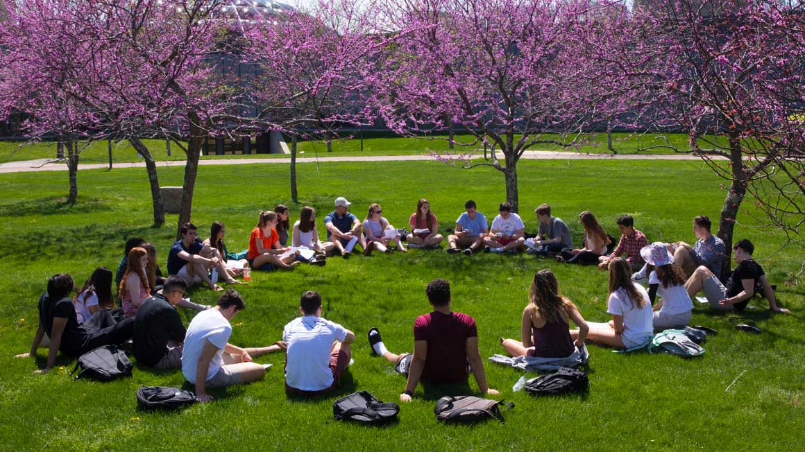 A group of students sit in a circle on the grass of the 鶹Ӱ quad