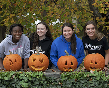 A group of four students stand behind the pumpkins they carved at 鶹Ӱ.