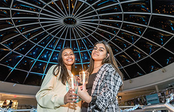 Two female students hold candles in the Rotunda during Festival of Lights, the holiday celebration at 鶹Ӱ.