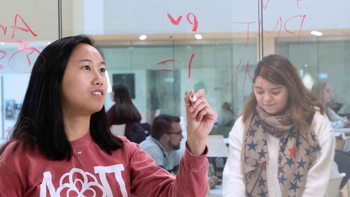 A Bryant student writes on the glass in one of the breakout rooms inside the Quinlan / Brown Academic Innovation Center.